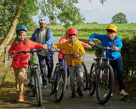 A group of children on bicycles being led by an adult on a scenic pathway.