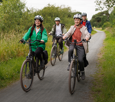 A group of people riding bicycles on a paved pathway through the countryside.