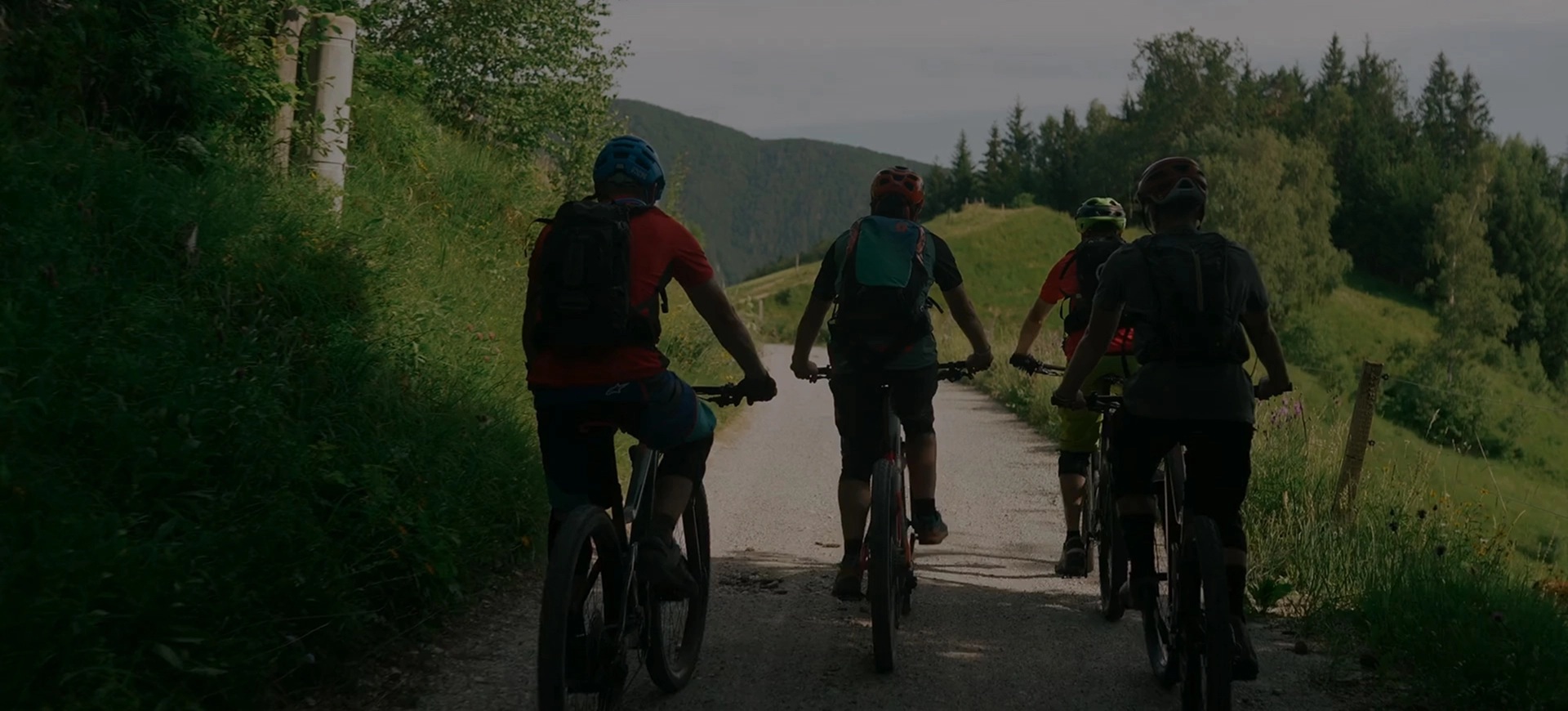 A group of cyclists ride together along a scenic countryside Greenway trail, enjoying an active outdoor adventure surrounded by rolling hills and woodland.