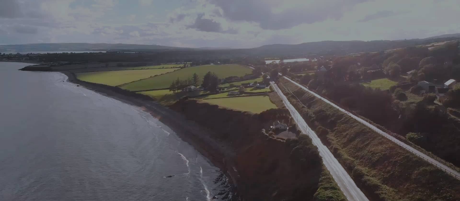 A stunning aerial view of the Waterford Greenway running alongside the coastline, showcasing scenic countryside, coastal cliffs, and sweeping views of the surrounding landscape.